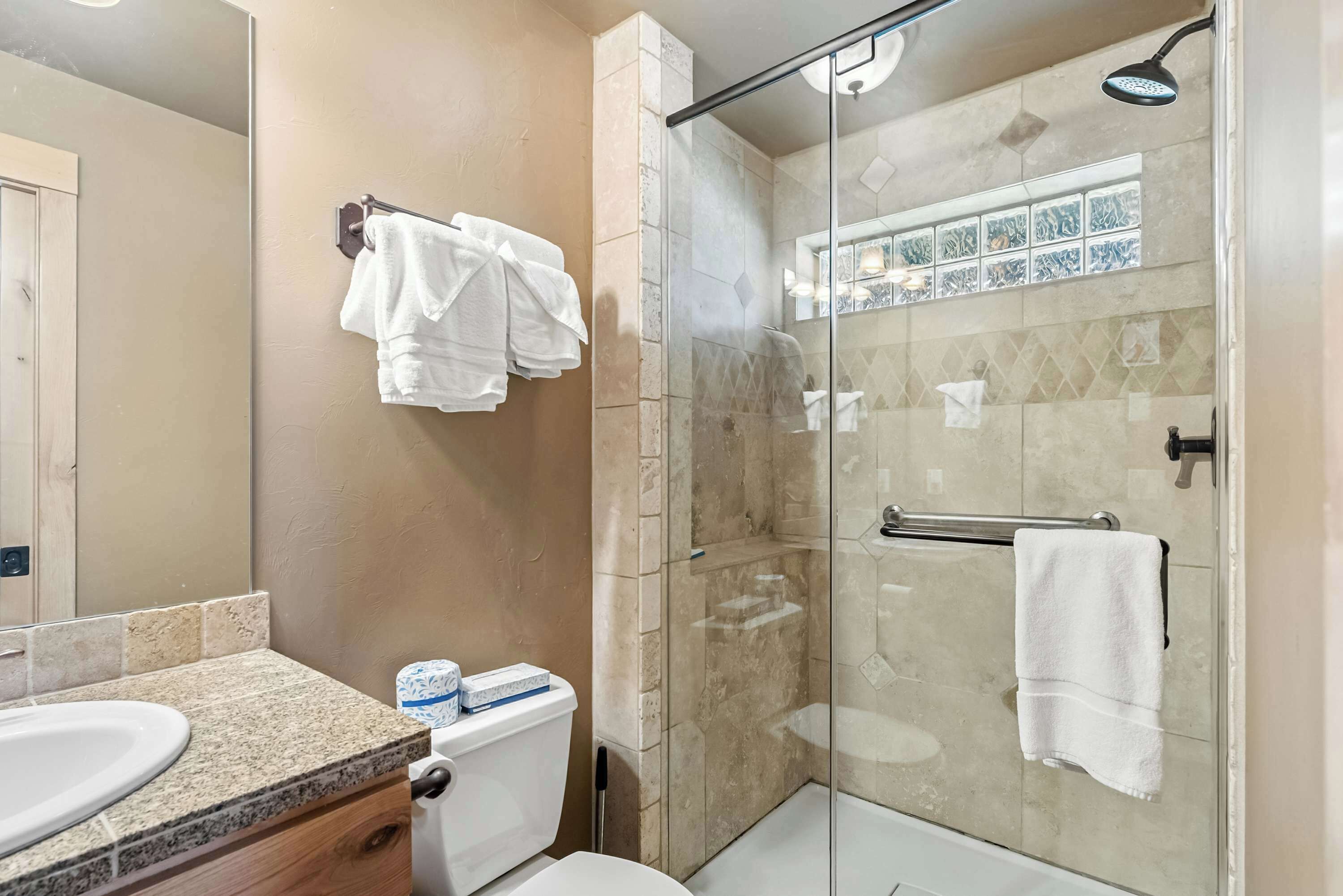 Un baño con ducha envuelta en vidrio, lavabo con encimera de granito y retrete.