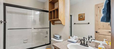 A bathroom with a shower, toilet, vanity, and a mirror.