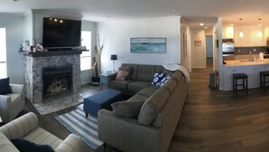A modern living room with a fireplace, a dining area with a large table and chairs, and a kitchen in the background. -  Beachfront, Beach Views, Great Location (Port St. Joe)