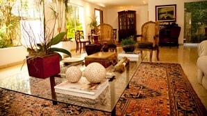 A spacious living room with a large window, a glass coffee table, and a variety of chairs and plants. - São Conrado Classy (Rio de Janeiro)