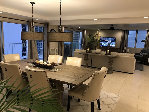 A modern dining area with a wooden table, beige upholstered chairs, and a decorative centerpiece. - Luxury Waikiki Penthouse - Ocean Views, Free Parking & WIFI (Honolulu)
