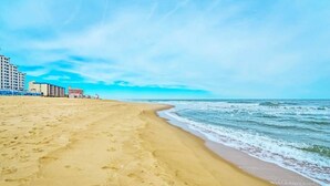 A sandy beach with footprints leading to the water, a clear sky, and buildings in the background. - SunburstParadise: LUX TH OceanView DOWNTOWN BOARDWALK 3BR 3BA with 2 Car Garage (Ocean City)