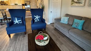 A living room with two blue armchairs, a grey sofa, and a coffee table with a basket of red roses. - SunburstParadise: LUX TH OceanView DOWNTOWN BOARDWALK 3BR 3BA with 2 Car Garage (Ocean City)