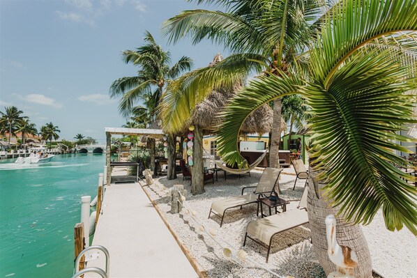 A beachside lounge with lounge chairs, a hammock, and a thatched-roof structure.