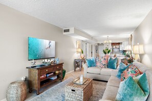 A living room with a television, sofa, coffee table, and decorative pillows.