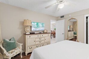 A bedroom with a bed, dresser, television, and a ceiling fan.