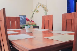 Une table à manger en bois avec quatre chaises, un vase blanc rempli de fleurs et un panneau noir avec un texte écrit à la craie.