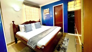 Une chambre à coucher avec un lit, une table de chevet, une fenêtre avec des rideaux, une porte et un mur orné d’un tableau.