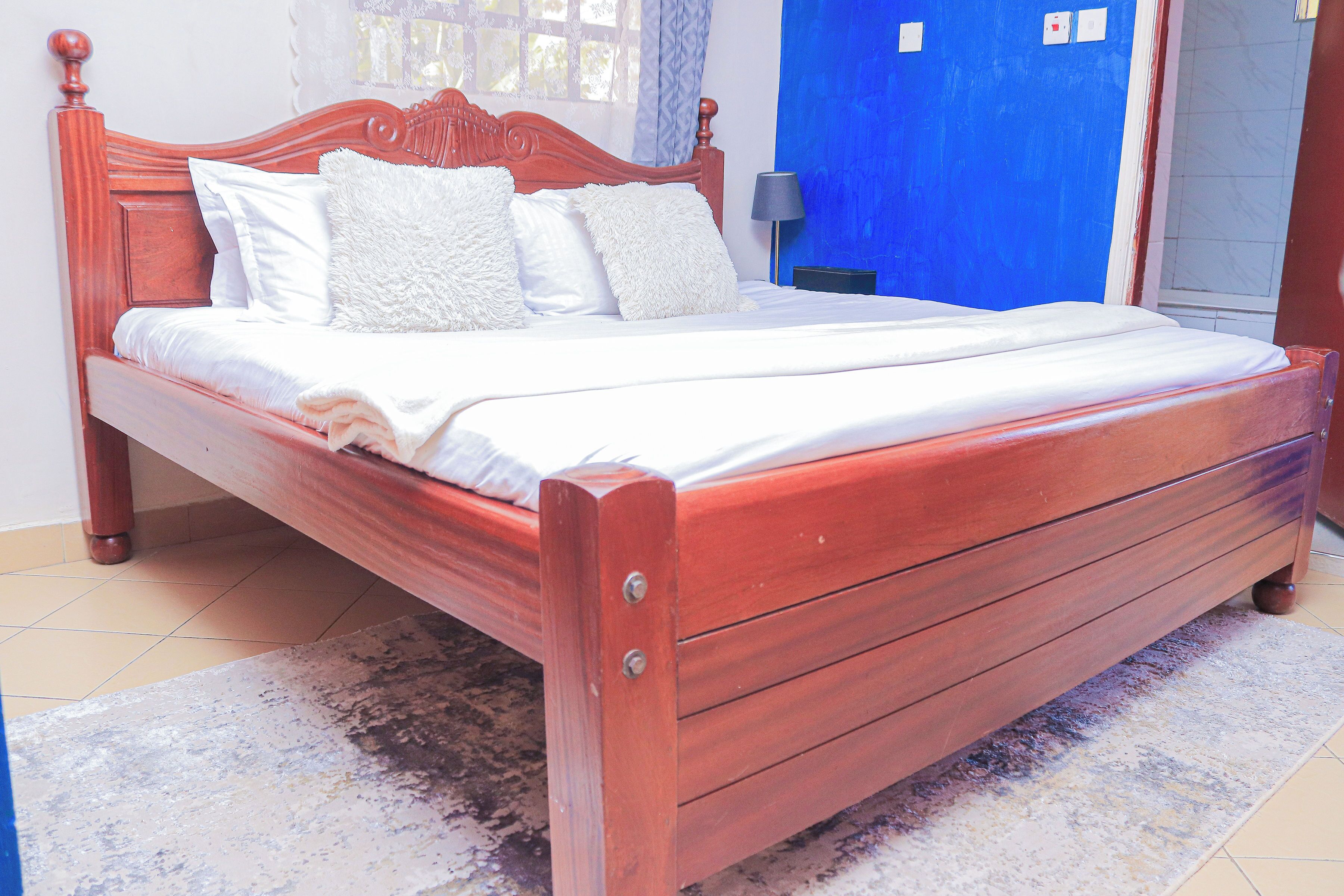 Un lit en bois avec une tête de lit, une literie blanche et un mur bleu en arrière-plan.