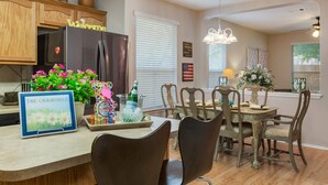A kitchen with wooden cabinets, a stainless steel refrigerator, a welcome sign, a potted plant, and a dining area with a table and chairs.