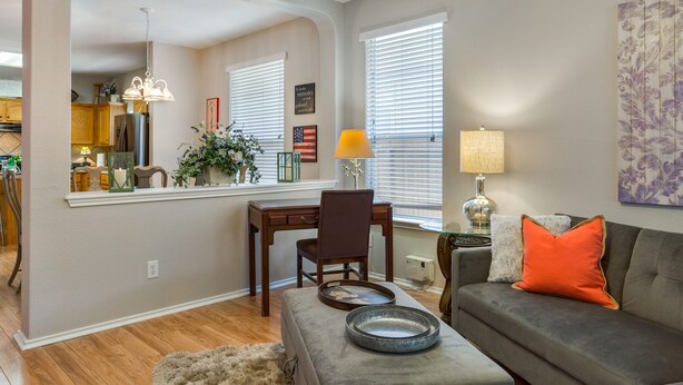 A living room with a gray sofa, a wooden coffee table, and a dining area with a wooden desk and chair.
