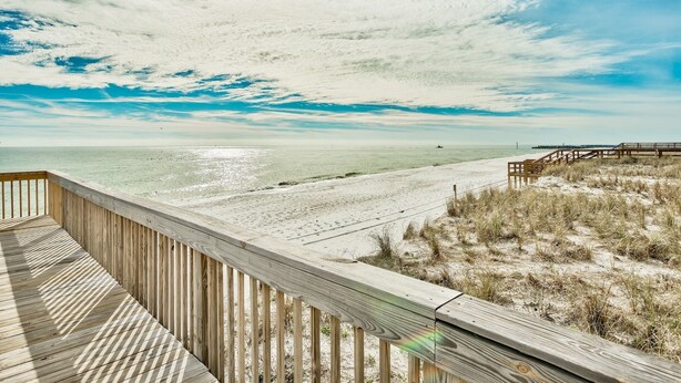 A wooden deck overlooking a beach with a wooden pier in the distance. - Sunset Jetty View! Enjoy one free beach chair set up and umbrella each day of yo (Destin)