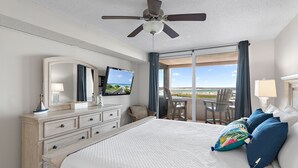 A hotel room with a bed, a television, a dresser, and a balcony with a view of the beach. - Sunset Jetty View! Enjoy one free beach chair set up and umbrella each day of yo (Destin)