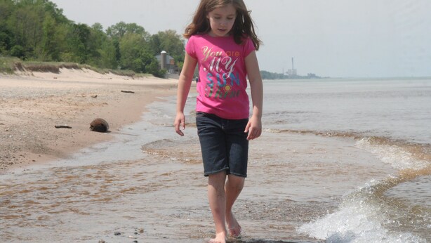 A beach scene with a child walking in shallow water.