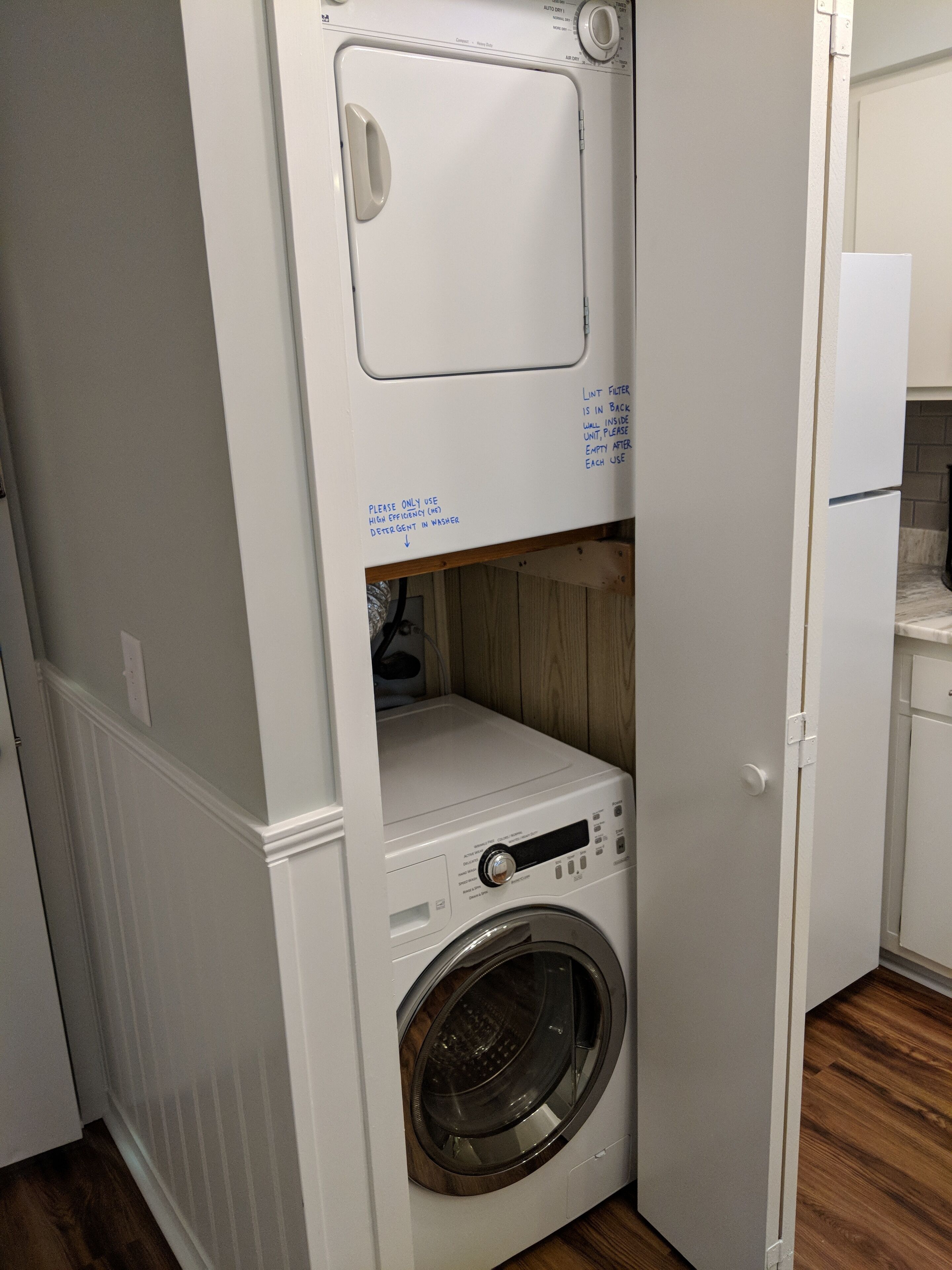 A compact laundry room with a front-loading washing machine, a lint filter compartment, and a small shelf.