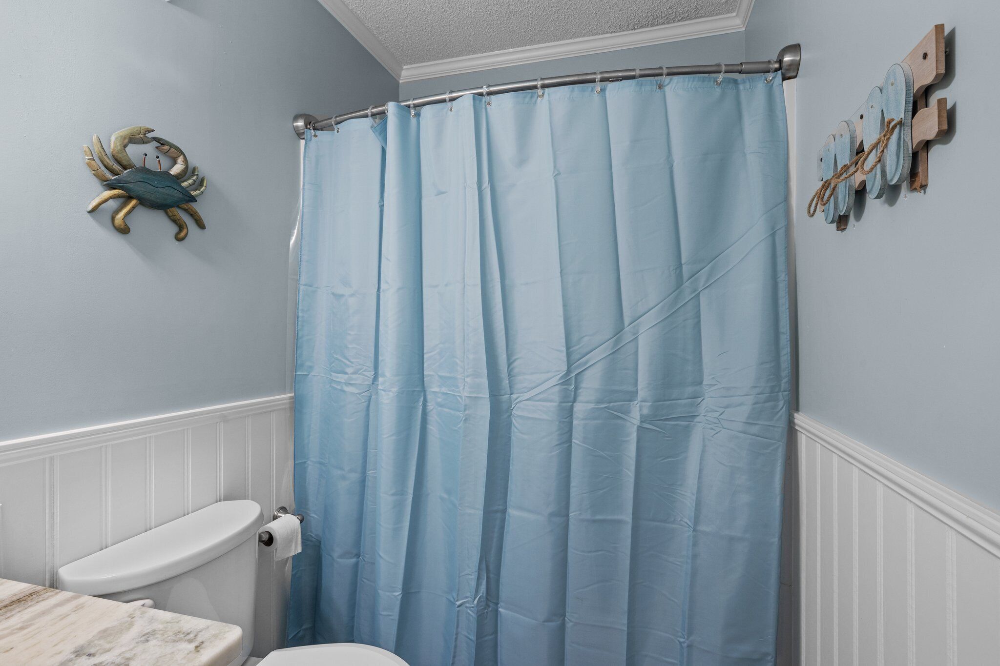 Une salle de bain avec un rideau de douche bleu, des toilettes et une décoration murale représentant un crabe.
