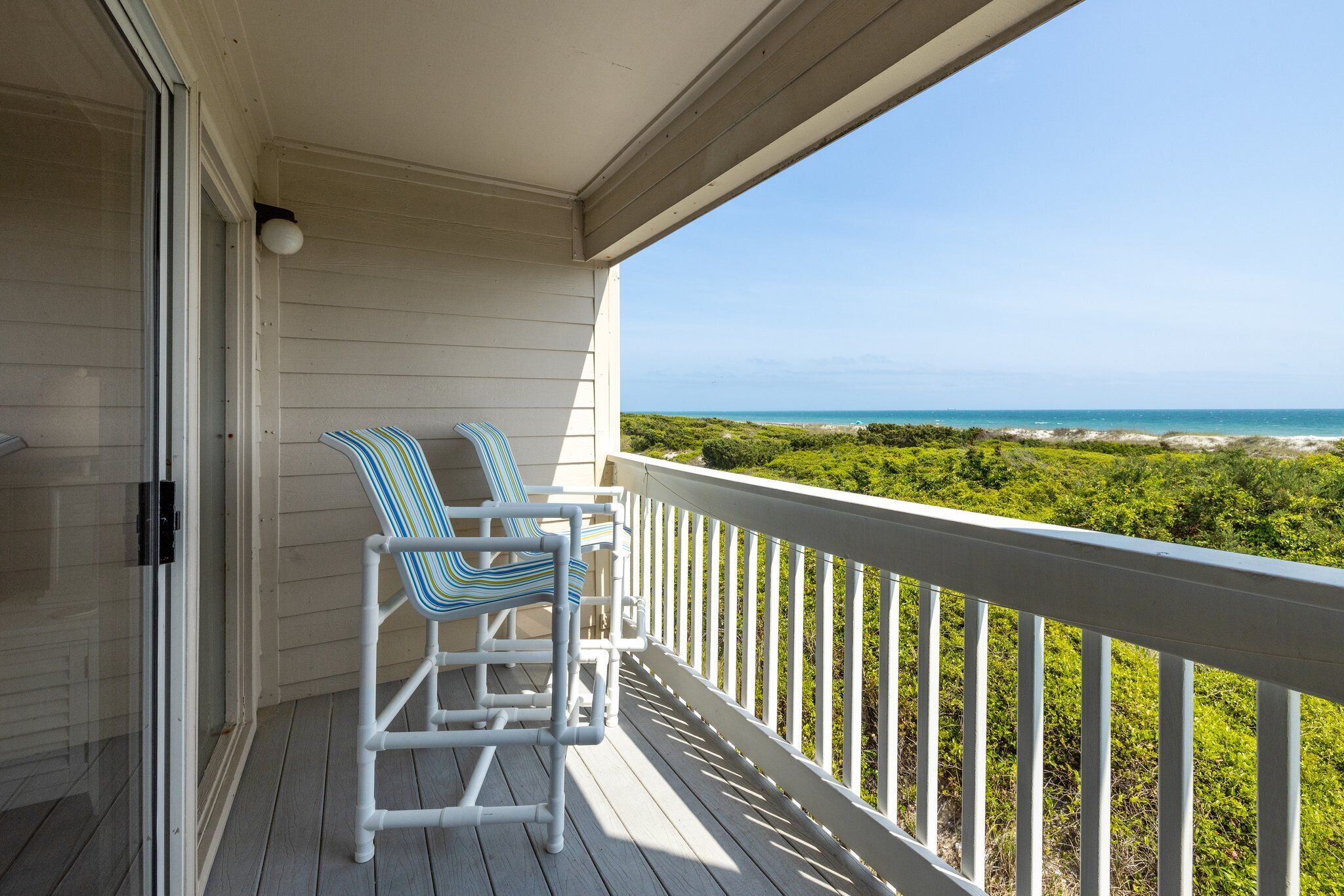 A balcony with a white railing overlooking a beach.
