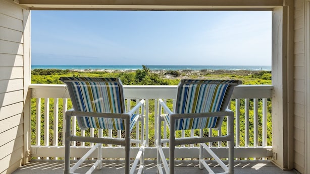 A porch with two striped chairs facing a view of the ocean and greenery. - Direct OCEAN FRONT CONDO gorgeous view A Place at the Beach, Beautifully Updated (Atlantic Beach)