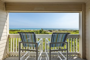 A porch with two striped chairs facing a view of the ocean and greenery.