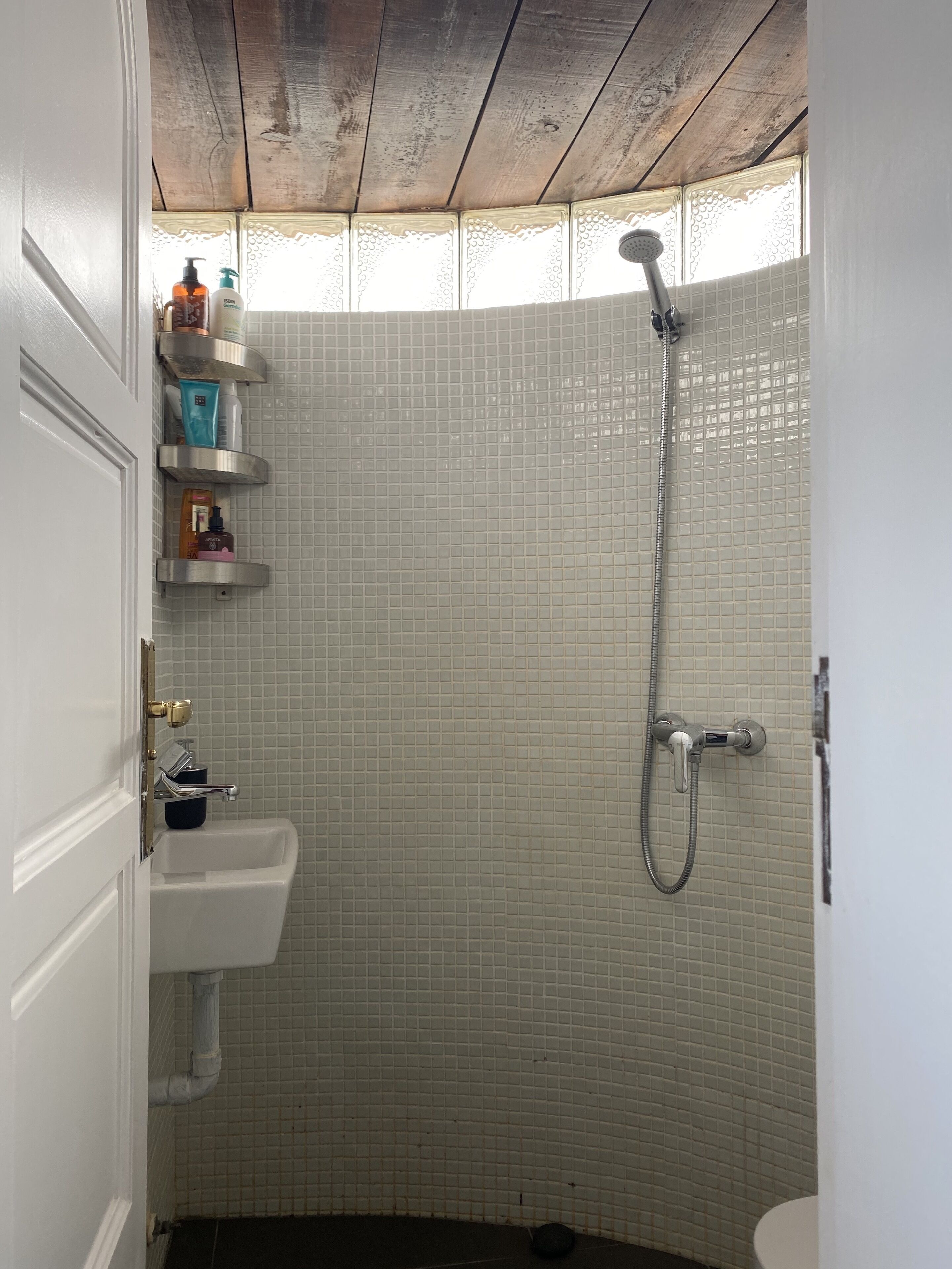 Een badkamer met een douche, wastafel en toilet. Er zijn planken met toiletartikelen.