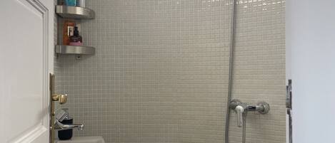 Een badkamer met een douche, wastafel en toilet. Er zijn planken met toiletartikelen.