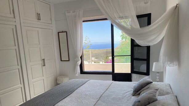 Un dormitorio con una cama grande, una ventana con vista al mar y cortinas blancas.