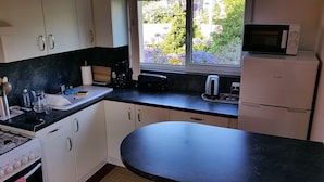 A compact kitchen with white cabinets, a black countertop, a stove, a microwave, and a window with a view of greenery.