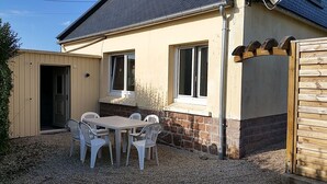 A house with a patio area featuring a table and chairs, a wooden gate, and a window with shutters.