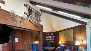 A cozy living room with a fireplace, wooden beams, a television, and a bookshelf. - Lakeview Capone Getaway, great sledding on property, fun loft for kids, Lg deck (Soda Springs)