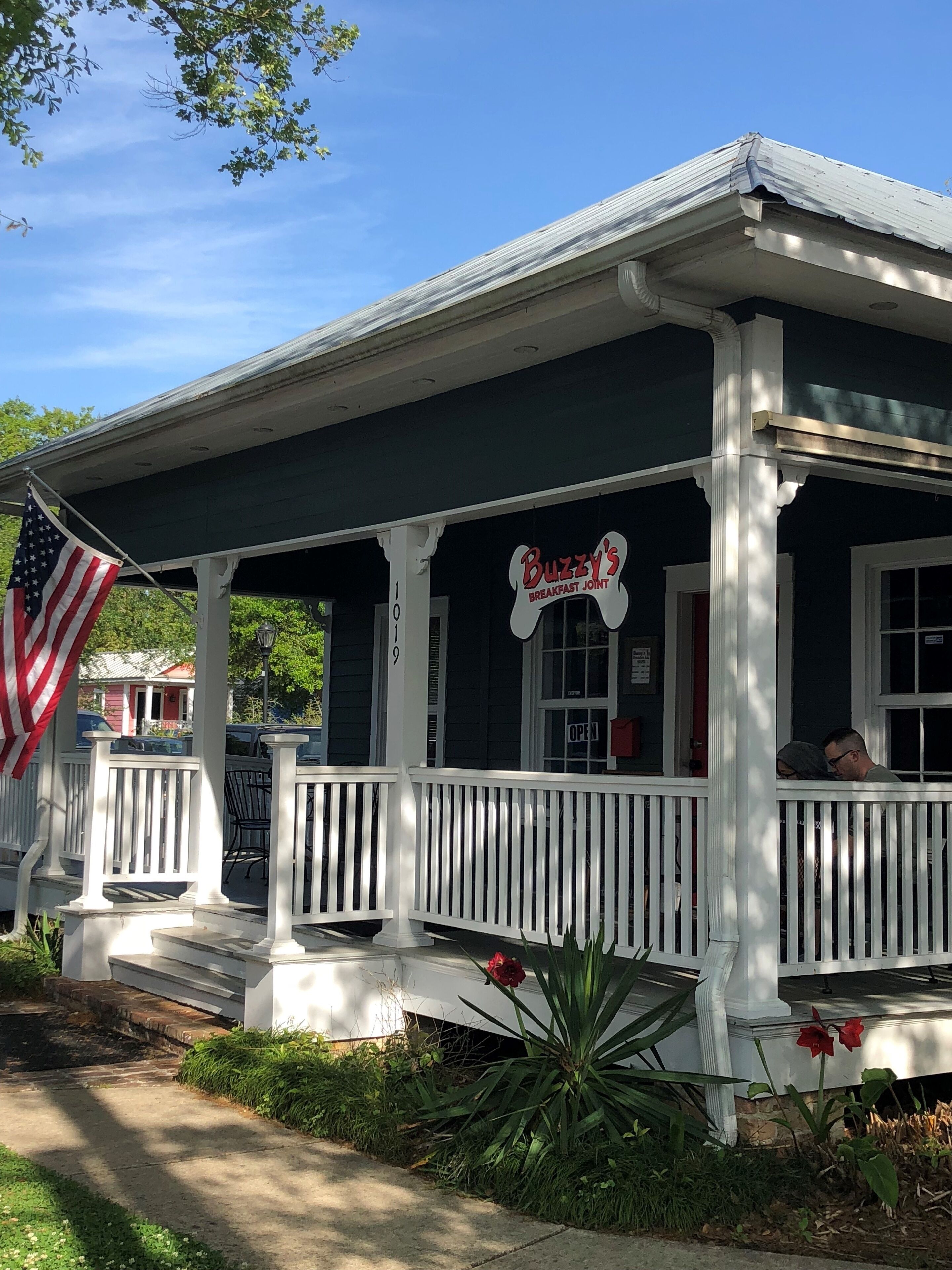 En toetagers bygning med en veranda, et amerikansk flag og et skilt, der siger "Buzzy's Breakfast Joint".