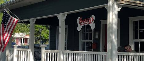 En toetagers bygning med en veranda, et amerikansk flag og et skilt, der siger "Buzzy's Breakfast Joint".