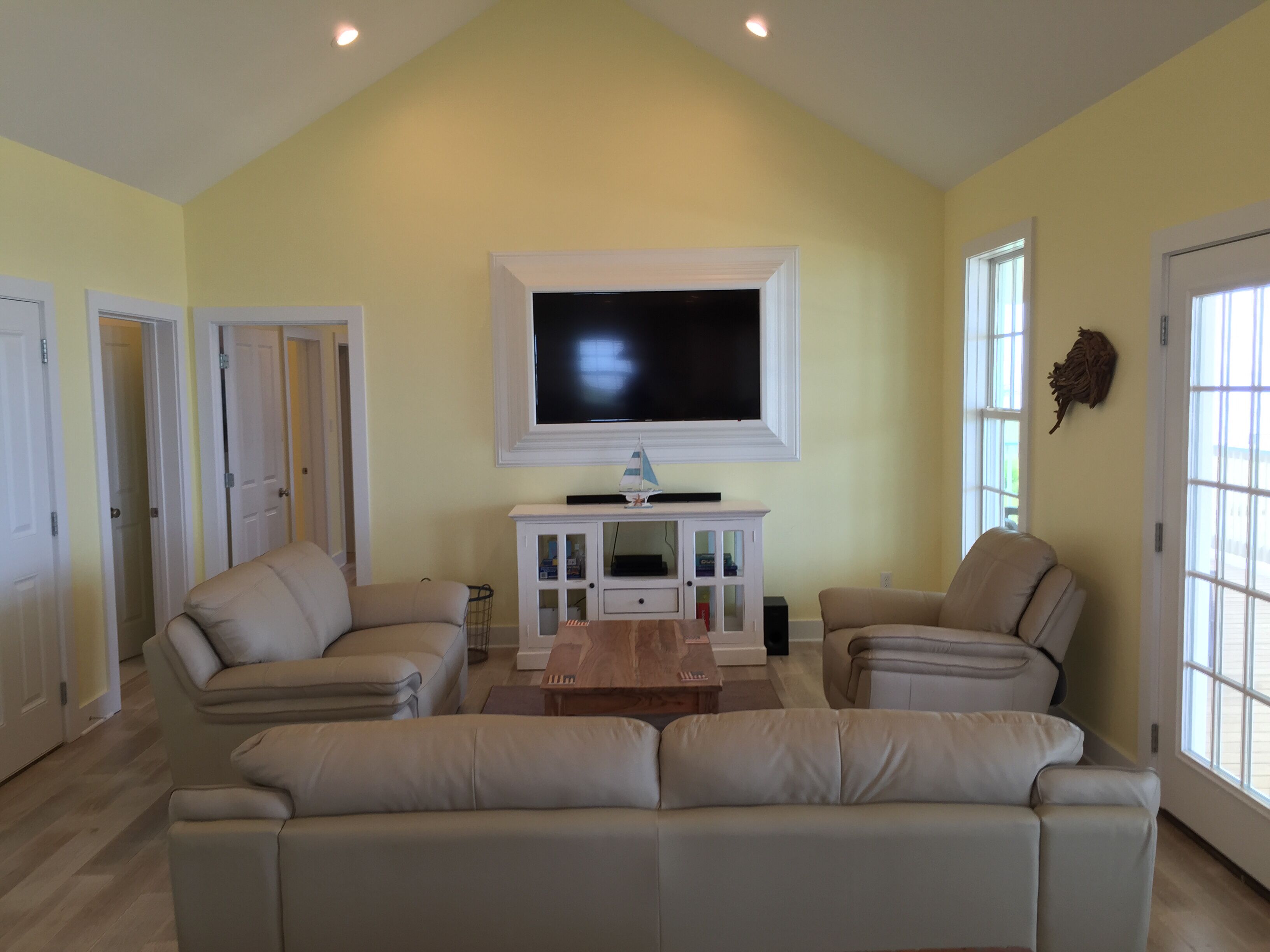 A living room with a large flat-screen TV, beige sofas, and a wooden coffee table.