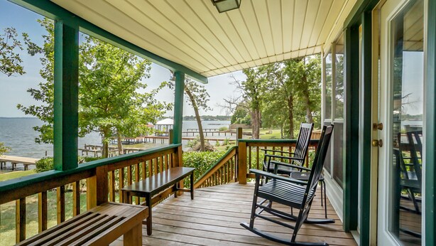 A wooden deck with a railing, benches, and a rocking chair overlooking a body of water.