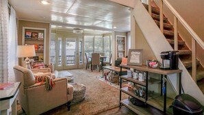 A living room with a sofa, coffee table, and a bookshelf. There is a staircase to the right.
