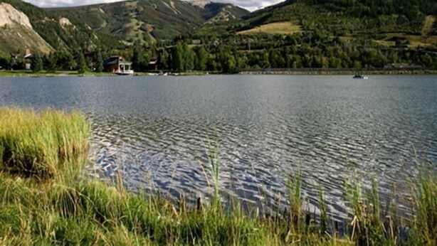 Ein See mit einem kleinen Haus am Ufer, umgeben von Hügeln und Grünflächen.