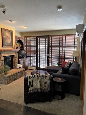 Cozy living room with a fireplace, sofa, and coffee table, featuring a stone fireplace and television.