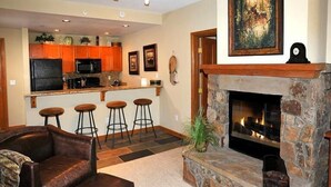 Ein Wohnzimmer mit Kamin aus Stein, Ledermöbeln und einer Küche im Hintergrund.
