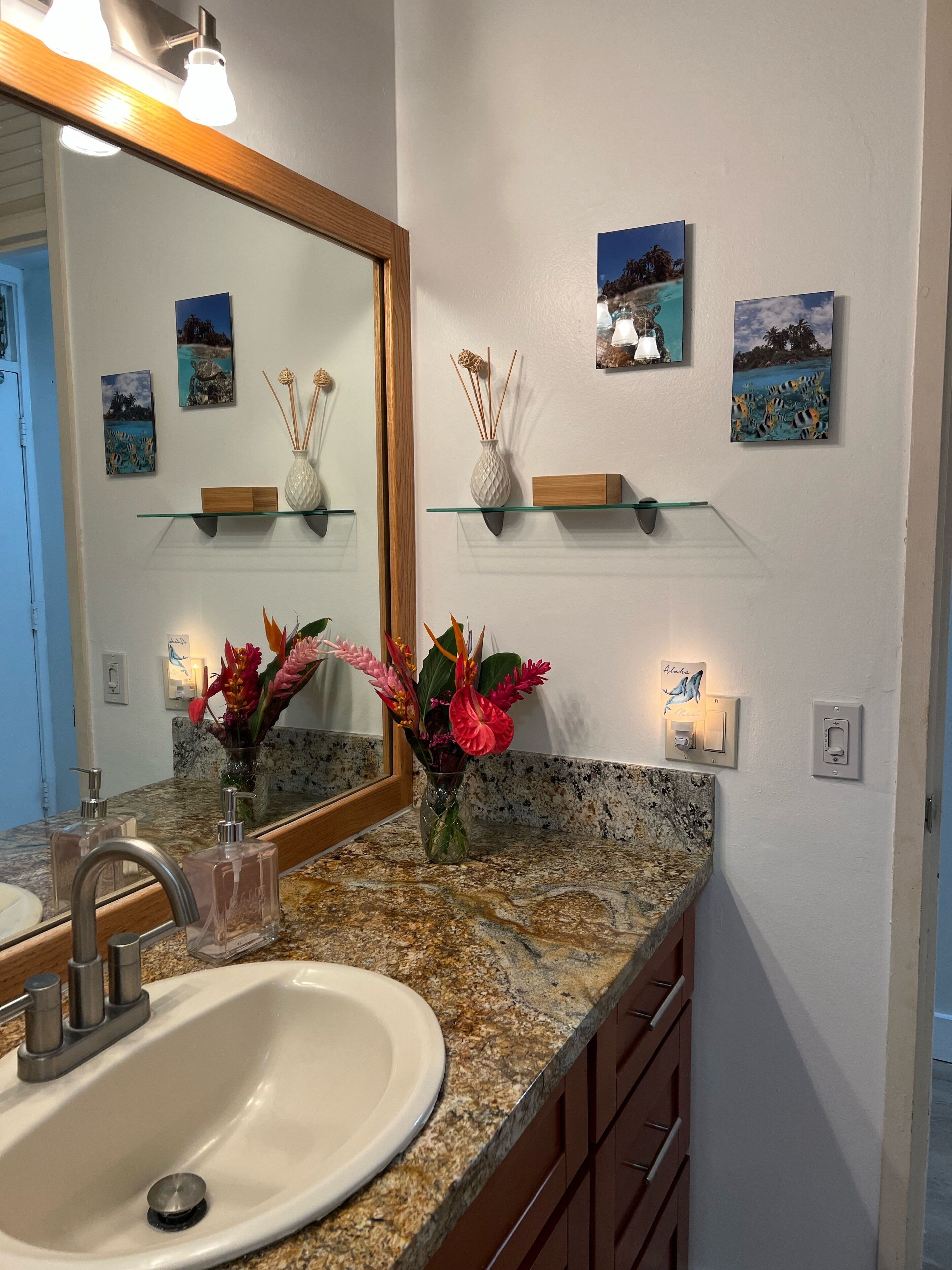 A bathroom with a granite countertop, a white sink, a mirror, and wall-mounted shelves with decorative items.