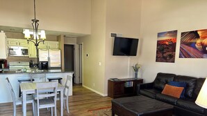 Una cocina moderna con comedor, una sala de estar con sofá de cuero y un televisor de pantalla plana montado en la pared.