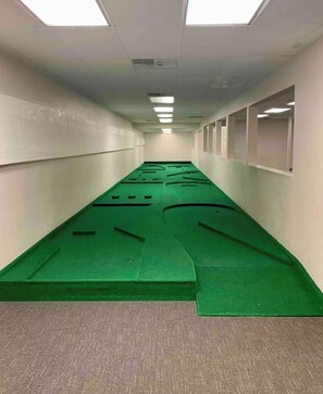 Un couloir avec des tapis verts sur le sol, des murs blancs et un plafond équipé de néons.