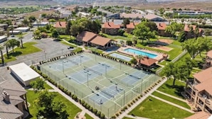 Una cancha de tenis rodeada de edificios residenciales, una piscina y un cielo despejado.