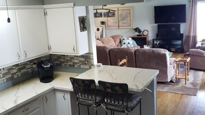 A compact living space with a kitchen area featuring white cabinets, a coffee maker, and a marble countertop. There is a dining table with chairs, a sofa, and a television in the living area. - Beautiful Waterfront Home on Baugo Bay (Osceola)