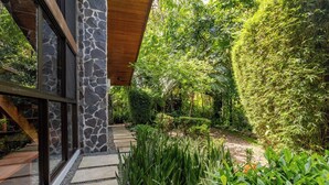 A modern building with stone and glass exterior, surrounded by lush greenery and a stone pathway. - Walk to Beach + Shops ~Pool, AC & Concierge (Uvita)