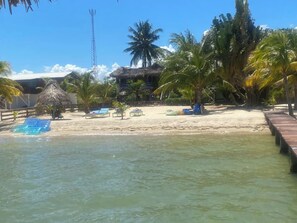 Ein Strand mit klarem Wasser, Palmen, einer strohgedeckten Hütte und einem Holzsteg.