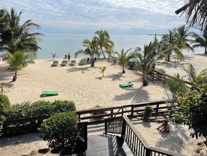 Una playa con palmeras, sillas de descanso y una terraza de madera.