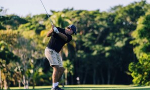 A person playing golf on a course with trees in the background.
