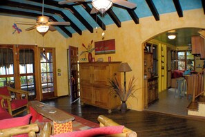 A spacious living area with wooden furniture, a ceiling fan, and a large window. - Beach House with Paddle Boards & Water Toys (Maya Beach)