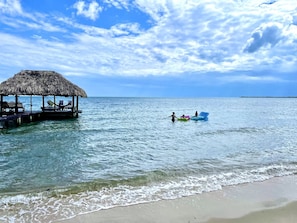 A beach with a thatched-roof structure and a pier with seating.