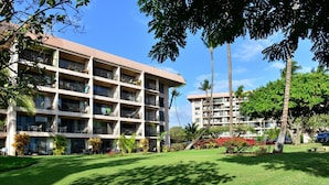 A multi-story hotel with balconies, a well-maintained lawn, and palm trees.