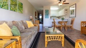 A living room with a sofa, coffee table, and dining area with chairs. There is a kitchen in the background.